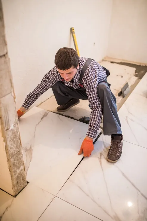Faianțar care pune plăci mari de gresie pe adeziv într-un apartament în renovare
